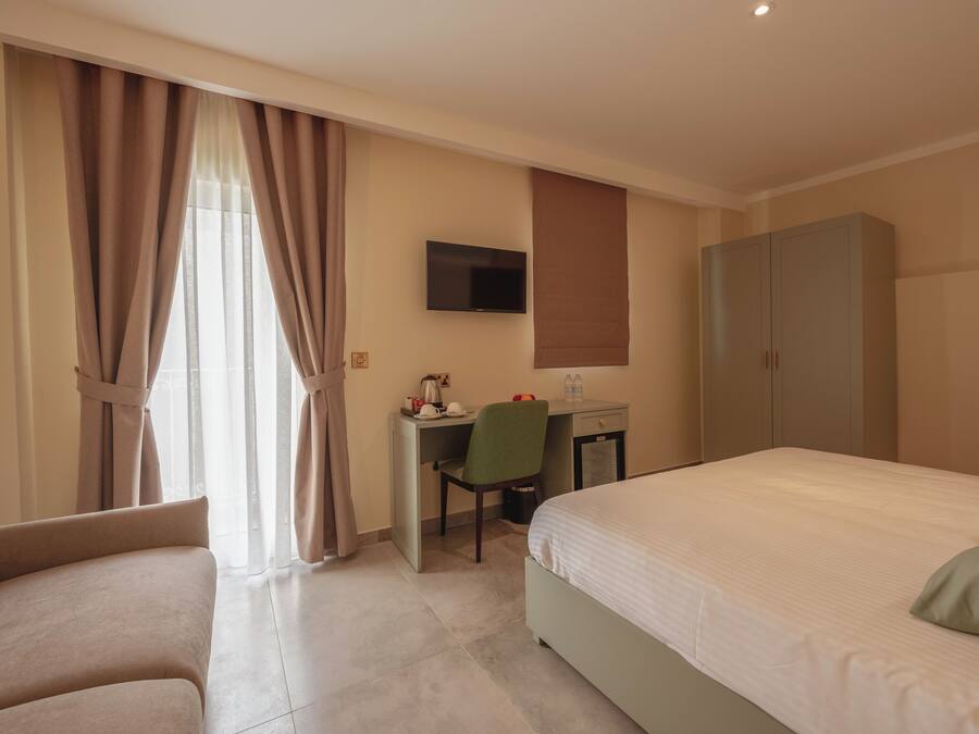 A hotel room with a bed, a desk with a chair, a television, and a wardrobe.