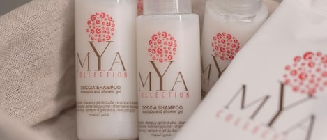 A set of four bottles and a packet of shampoo labeled 'MYA COLLECTION' with a red logo, placed on a beige cloth.