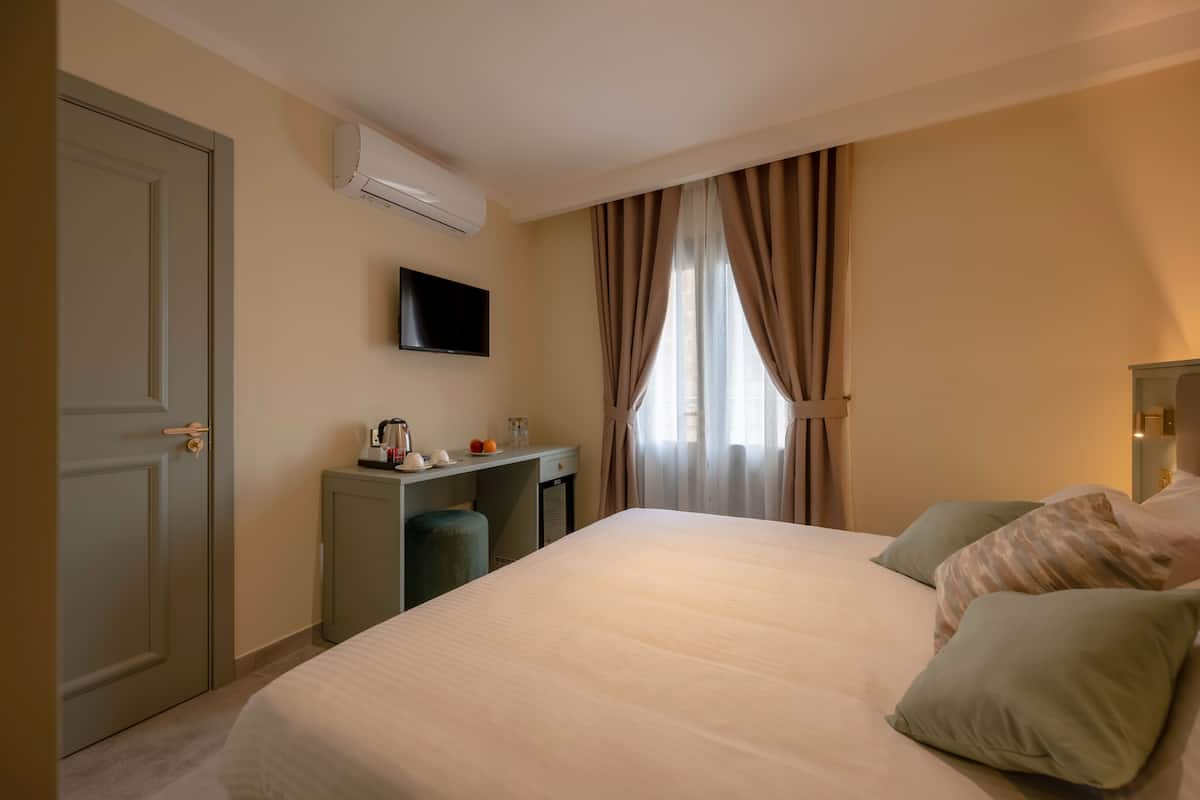 Una habitación de hotel con cama, escritorio, televisor y ventana con cortinas.
