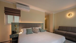 Una habitación de hotel con una cama grande, un sofá, una mesita de noche con teléfono y un equipo de aire acondicionado.