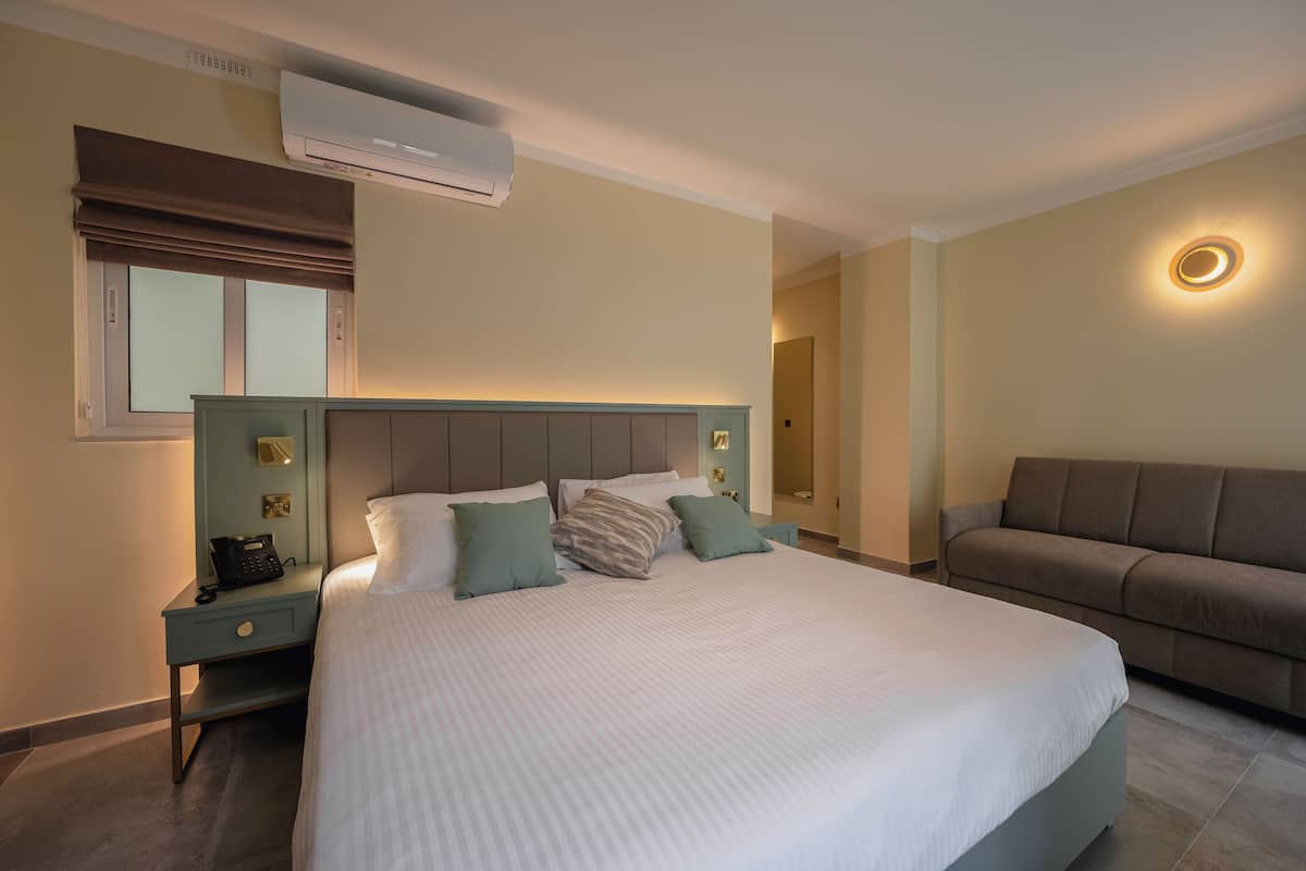 Una habitación de hotel con una cama grande, un sofá, una mesita de noche con teléfono y un equipo de aire acondicionado.