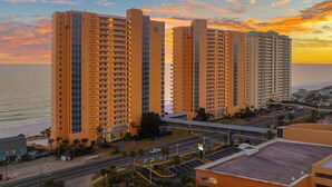 Un hotel de gran altura con varios pisos, un puente peatonal y vista al océano al atardecer.