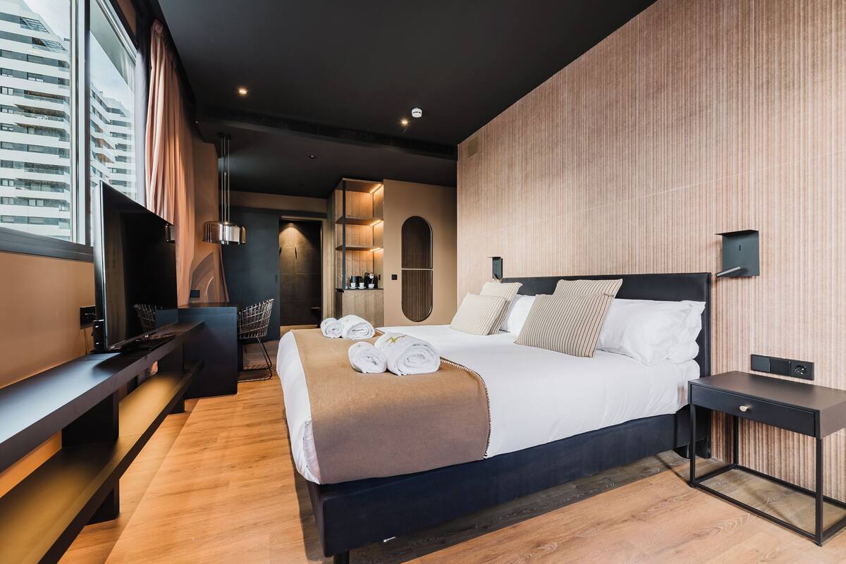 A modern hotel room with a large bed, a desk, and a view of the city.