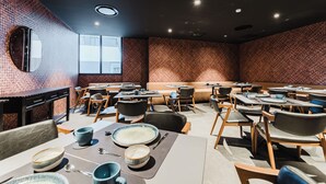 A modern restaurant with brick walls, round tables, and black chairs. - Hotel Arena Select (València)