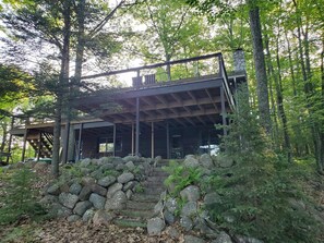A cabin with a stone staircase leading up to a wooden deck, surrounded by trees.
