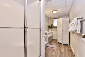 A compact bathroom with a shower, toilet, and sink, a towel rack, and a small potted plant.