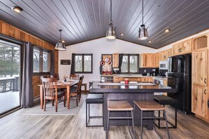 A modern kitchen with wooden cabinets, a central island, and a dining area with a table and chairs. - Boulder Lakefront and Bike Trail Access (Boulder Junction)