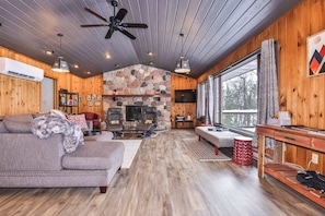A cozy cabin interior with a stone fireplace, wooden walls, a sofa, and a television.