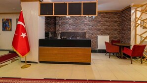 Een receptiegedeelte met een bakstenen muur, een receptiebalie, rode stoelen en een vlag.