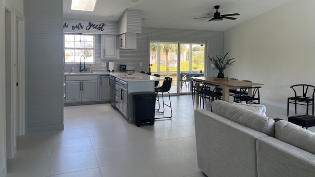 A modern kitchen with white cabinets, a central island, and a dining area with a table and chairs. - Salty Waterways Escape with a dock. Family friendly, boat rental available  (Palm Coast)