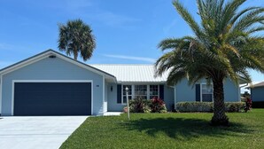 A single-story house with a garage, a well-maintained lawn, and a palm tree. - Salty Waterways Escape with a dock. Family friendly, boat rental available  (Palm Coast)