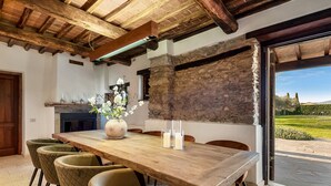 Un comedor con una mesa de madera, seis sillas, un jarrón con flores y una pared de piedra.