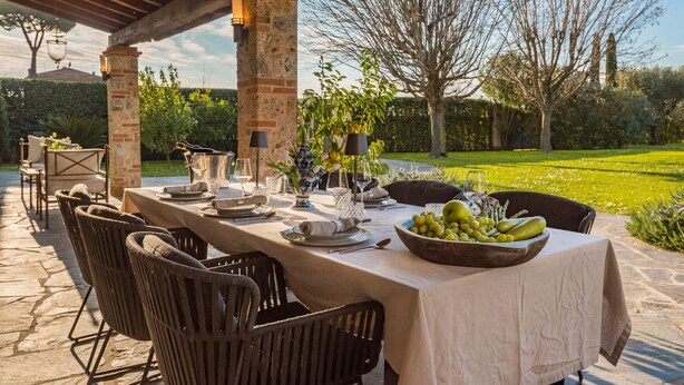Un área de comedor al aire libre con una mesa de piedra, sillas de mimbre y vistas a un jardín.