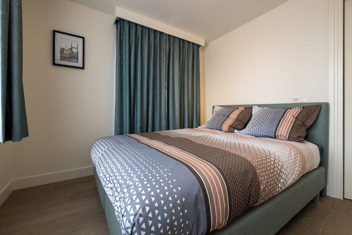 Een keurig opgemaakt bed met beddengoed met een patroon, een hoofdbord en een ingelijste foto aan de muur.
