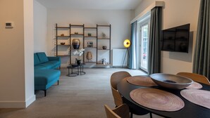 Un salon moderne avec un canapé de couleur turquoise, une table à manger agrémentée de sets de table et une étagère décorative où sont exposés divers objets.