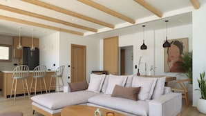 Una sala de estar moderna con un sofá modular, vigas de madera en el techo y una zona de comedor con taburetes de bar.