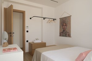 A bedroom with a bed, a bedside table, a hanging coat rack, a door, and a wall-mounted painting.