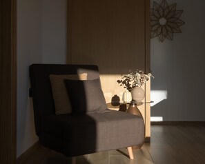 Uma sala de estar moderna com um sofá de cor escura, uma pequena mesa lateral com objetos decorativos e piso de madeira.