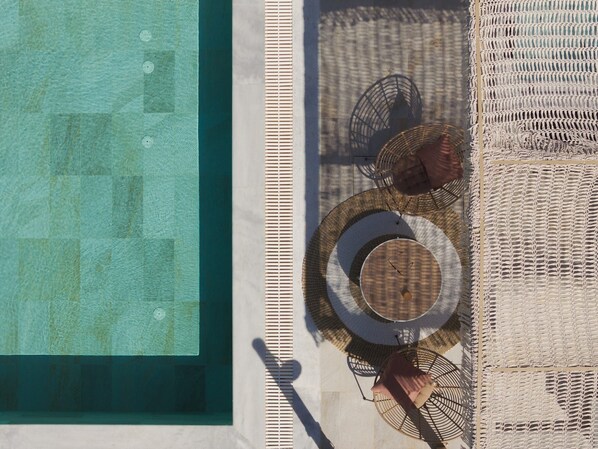 A rooftop pool area with a clear view of the pool, lounge chairs, and a woven table.