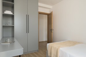 Quarto com cama, mesa de cabeceira, guarda-roupa e porta que dá para outro cômodo.