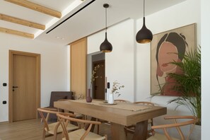 Ein Essbereich mit Holztisch und Stühlen, Pendelleuchten, einer Blumenvase und einem großen Gemälde an der Wand.