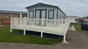 Une maison mobile de plain-pied, avec une façade blanche, un balcon doté d’une balustrade blanche et un petit porche.