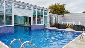 Une piscine à l’eau d’un bleu limpide, entourée d’un bâtiment doté de grandes fenêtres et d’une bordure carrelée.