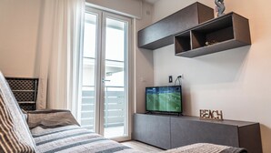 Une chambre moderne comprenant un lit, une télévision, une porte coulissante donnant sur un balcon et une étagère avec des objets décoratifs.