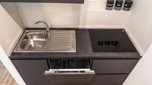 Une cuisine compacte dotée d’un évier en acier inoxydable, d’un lave-vaisselle et d’un plan de travail noir.