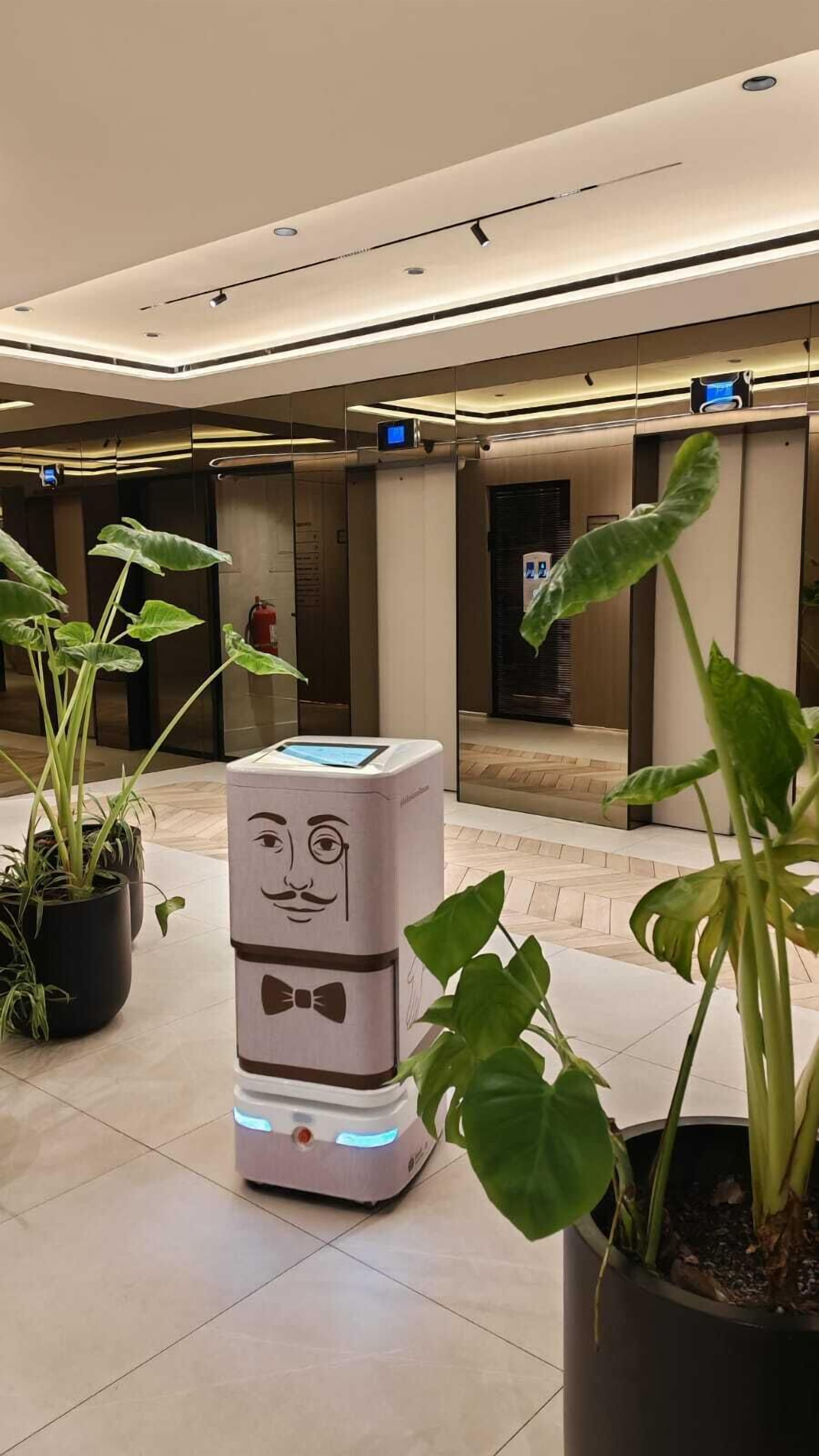 A modern lobby with a unique interactive kiosk, potted plants, and a clean, tiled floor.