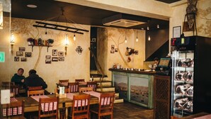 Ravintolassa on puupöytiä ja -tuoleja, baaritiski, jossa on esille tuotuja tuotteita, ja seinät on koristeltu kehystetyillä kuvilla.
