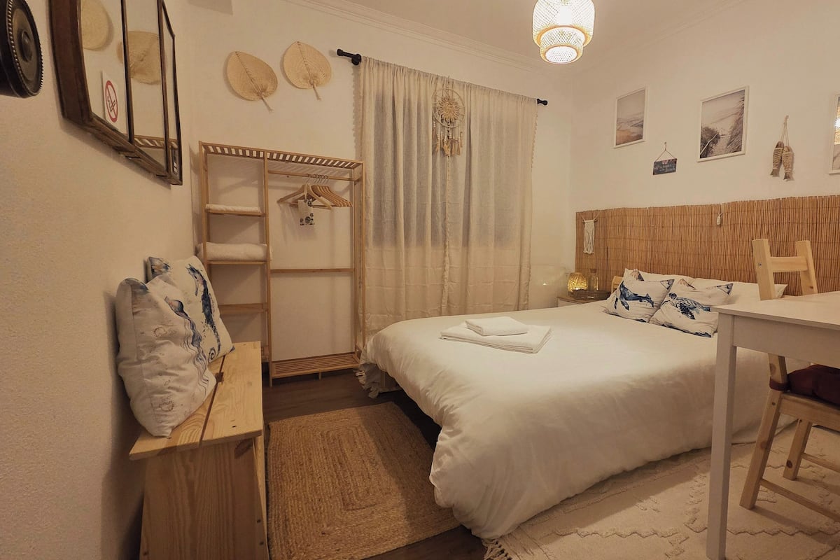 Un dormitorio ordenado con cama, mesita de noche y un pequeño escritorio.