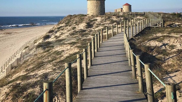 A wooden boardwalk leading to two stone towers with red roofs, overlooking a beach. - Guest House da Mata (A Ver-o-Mar)