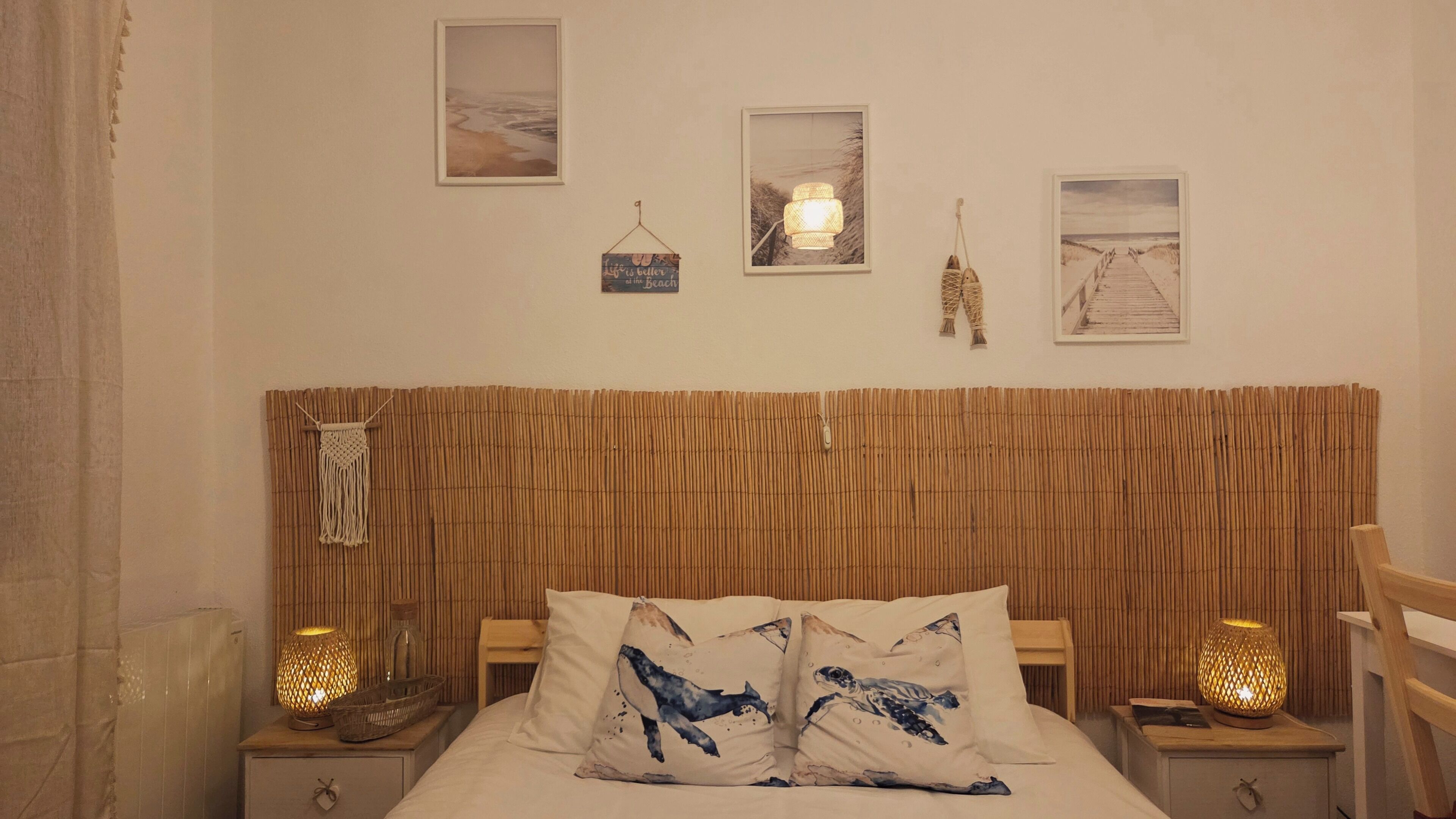 A bedroom with a bed, two nightstands, a wall-mounted lamp, and three framed pictures.