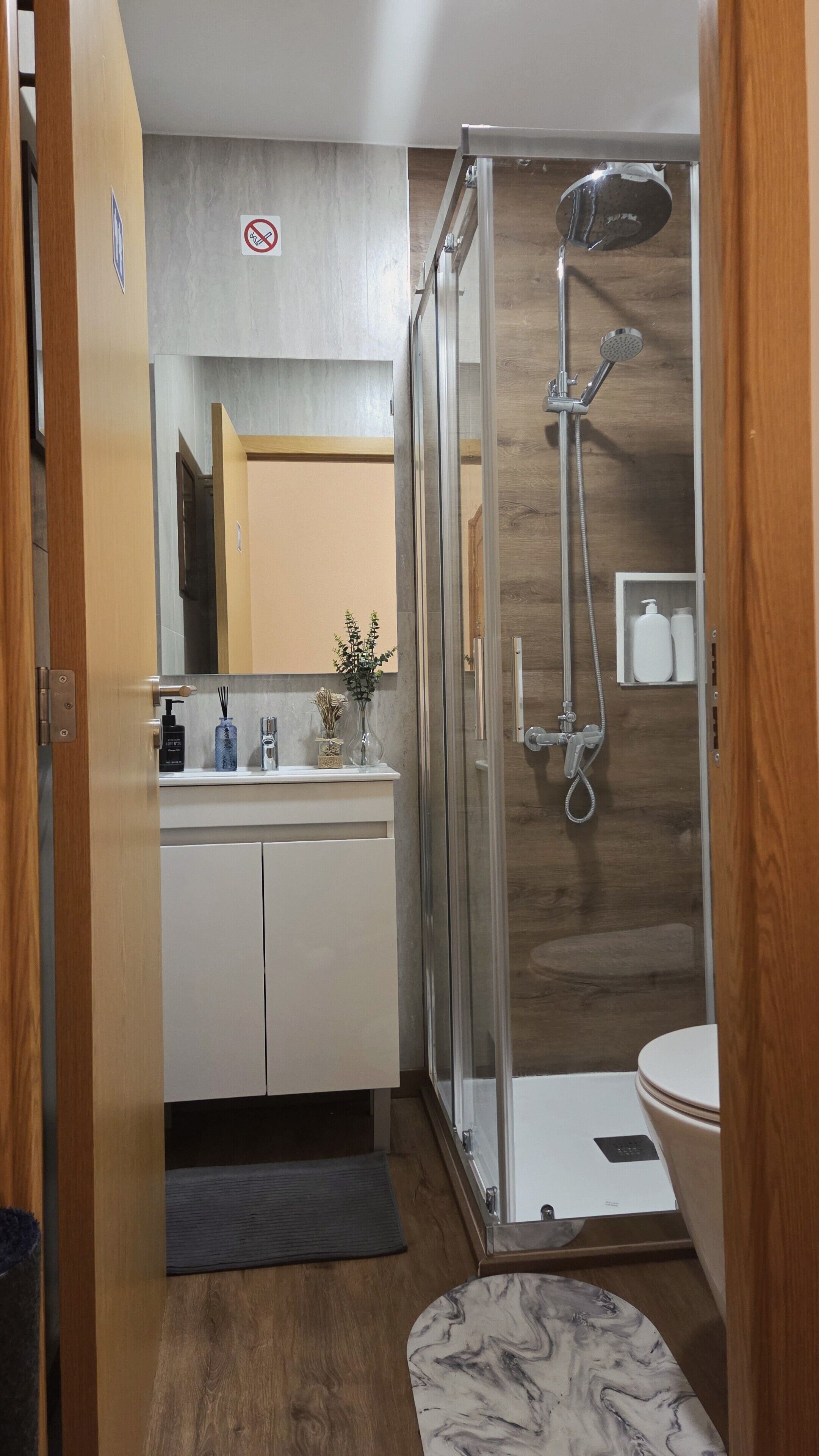 Ein modernes Badezimmer mit einer Duschkabine, einer weißen Toilette und einem Waschtisch mit Spiegel und Pflegeartikeln.