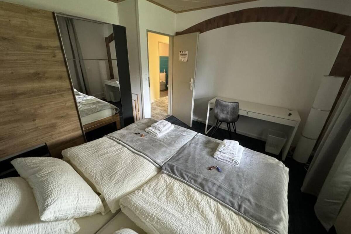 A hotel room with two beds, a desk, a chair, and a mirror.