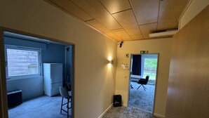 A hallway with a carpeted floor, a door leading to a room with a window and a radiator, and a chair in the adjacent room. - HubTime (Algermissen)