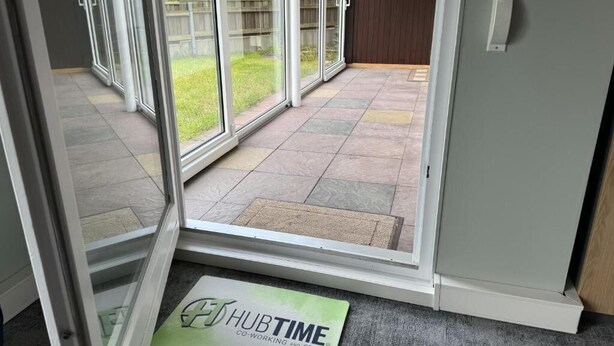 A hotel entrance with a sliding glass door leading to a patio area. - HubTime (Algermissen)