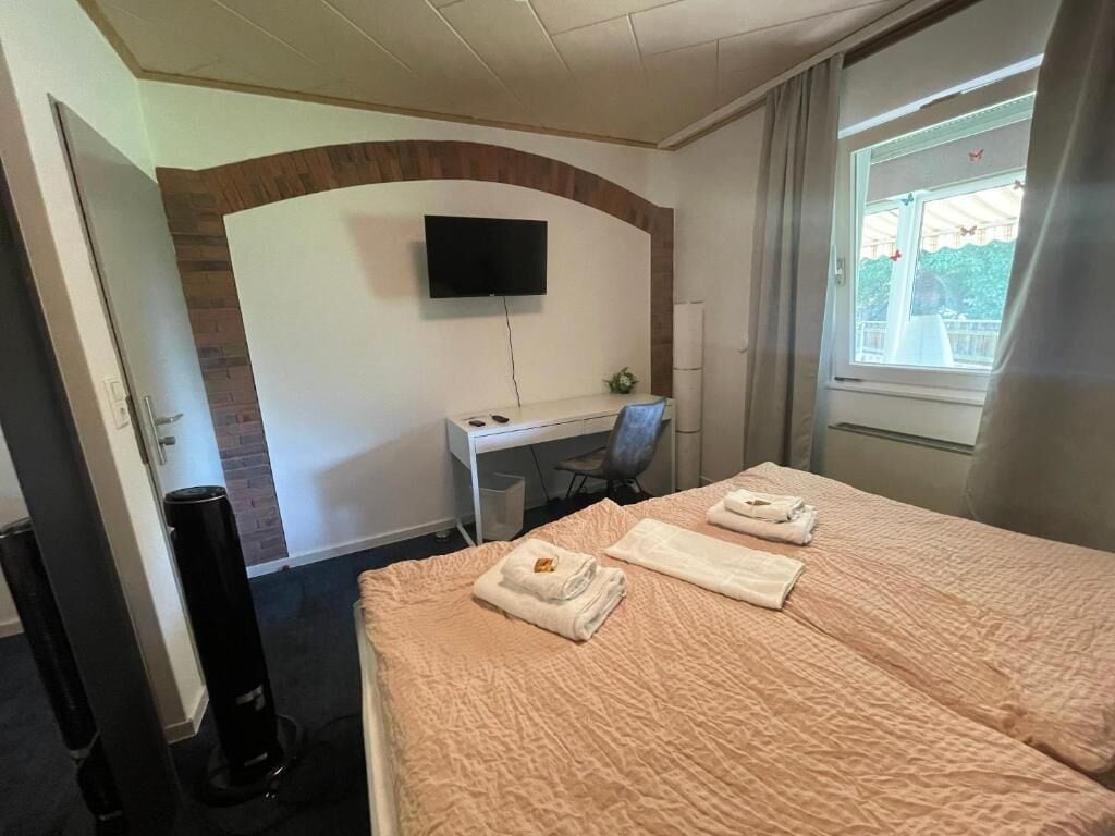 A hotel room with a bed, a desk, a chair, a TV, and a window with curtains.