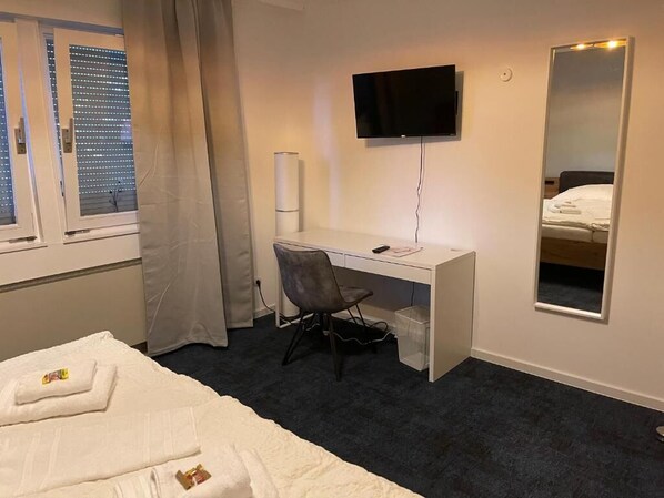 A hotel room with a bed, a desk, a chair, a TV, and a mirror. - HubTime (Algermissen)