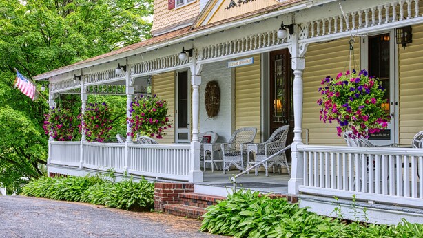 Un porche con sillas de mimbre, cestas de flores colgantes y un cartel que dice "BED AND BREAKFAST".