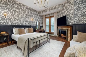 A bedroom with a bed, a fireplace, a television, and patterned wallpaper.