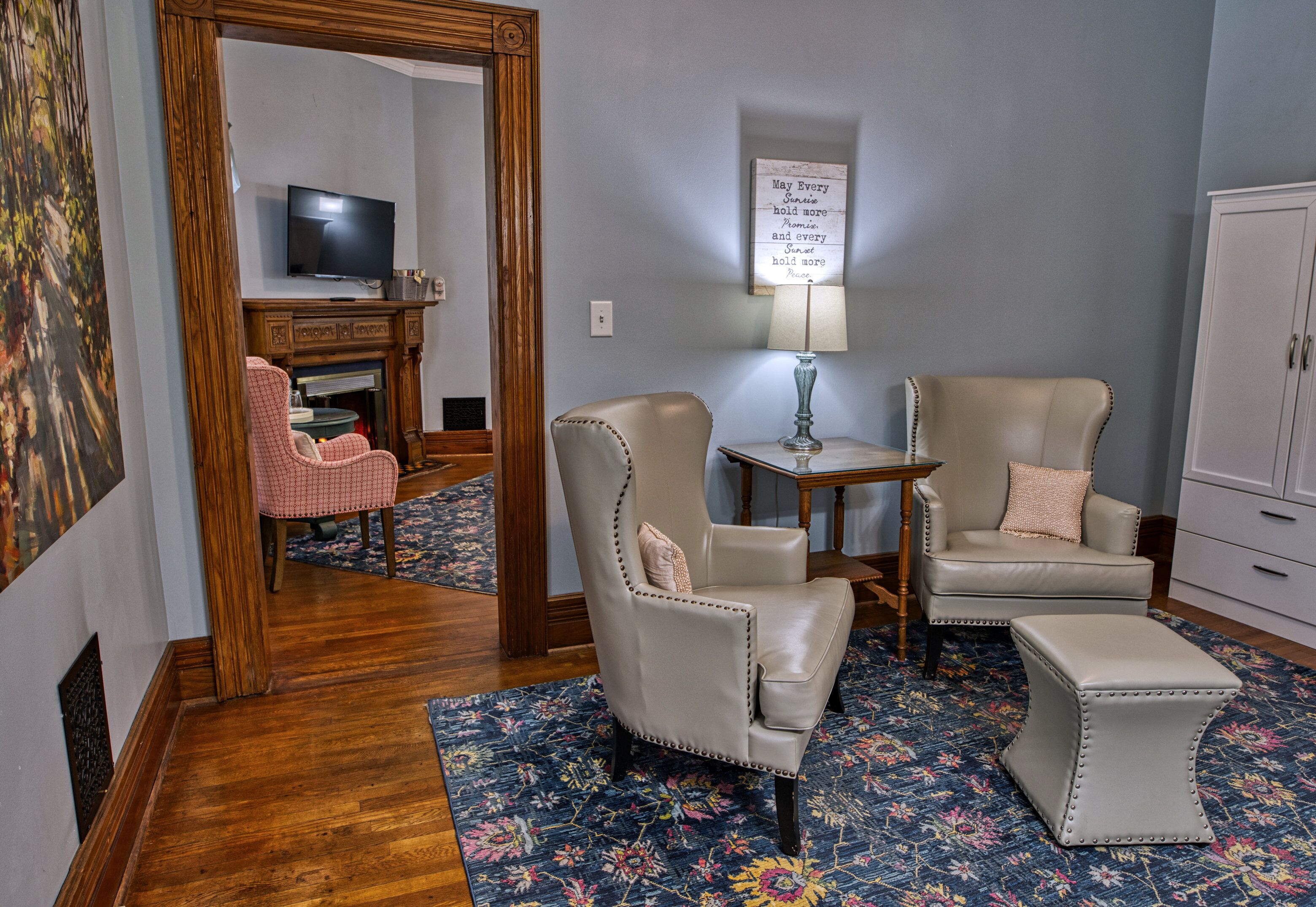 A room with two leather armchairs, a small table with a lamp, a television, and a cabinet.