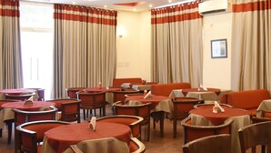 A hotel dining area with round tables and chairs, red and beige curtains, and a chandelier. - Surkhab Tourist Resort (Sirsa)