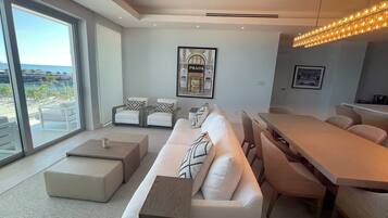 A modern living room with a large window, a sofa set, a dining area, and a framed picture on the wall.