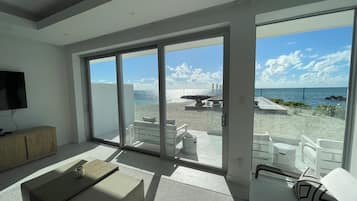 A modern living room with a large sliding glass door leading to a balcony with a view of the beach and ocean.