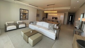Ein modernes Wohnzimmer mit einer Sofagarnitur, einem Couchtisch und einem Essbereich im Hintergrund.