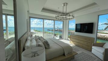 A modern bedroom with a large bed, a TV, and a view of the ocean.