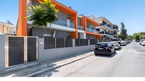 Un edificio residencial moderno de varios pisos con una fachada anaranjada llamativa, una entrada con portón y una fila de coches aparcados a lo largo de la calle.