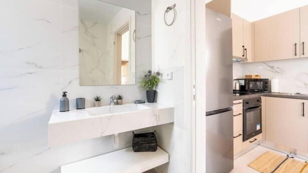 Un baño moderno con un espejo grande, dos lavamanos, un banco y una planta en maceta.